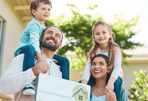 Une famille heureuse avec deux enfants et une pancarte « professionnel de l'immobilier » devant une maison, célébrant l'achat d'une nouvelle maison.