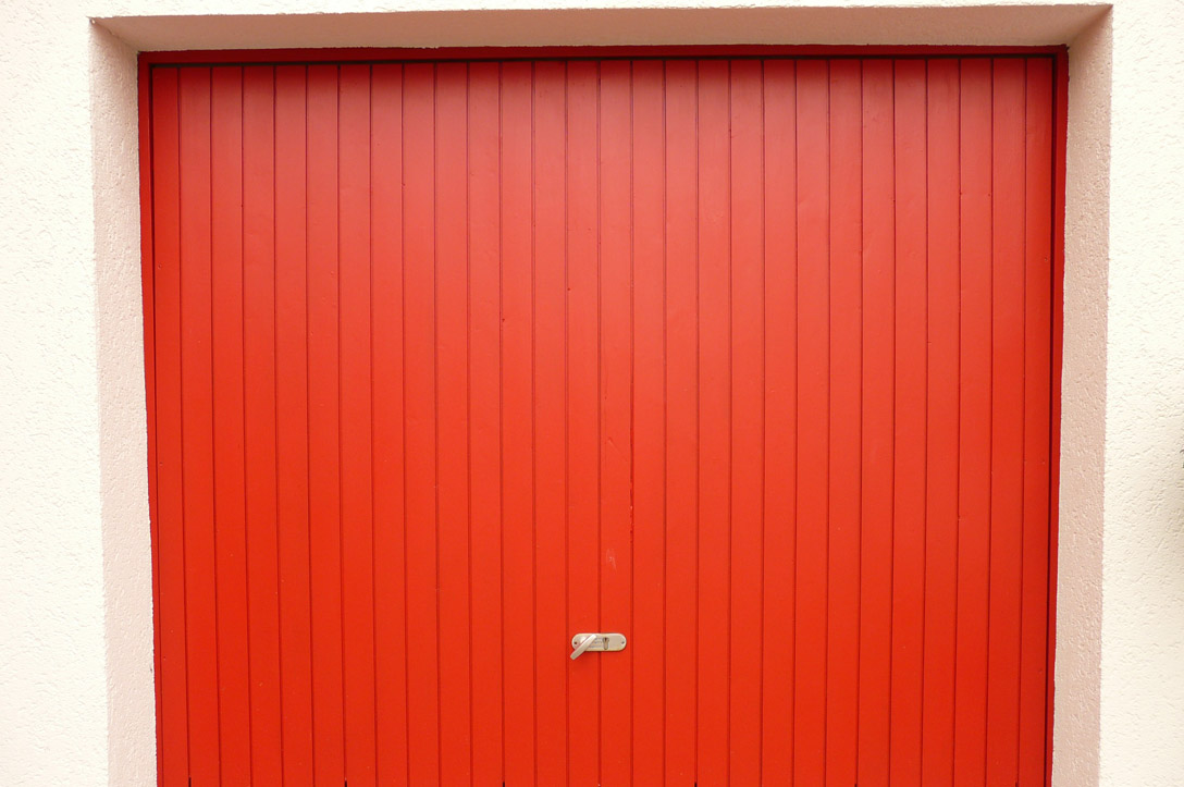 Porte de garage rouge fermée, composée de panneaux verticaux